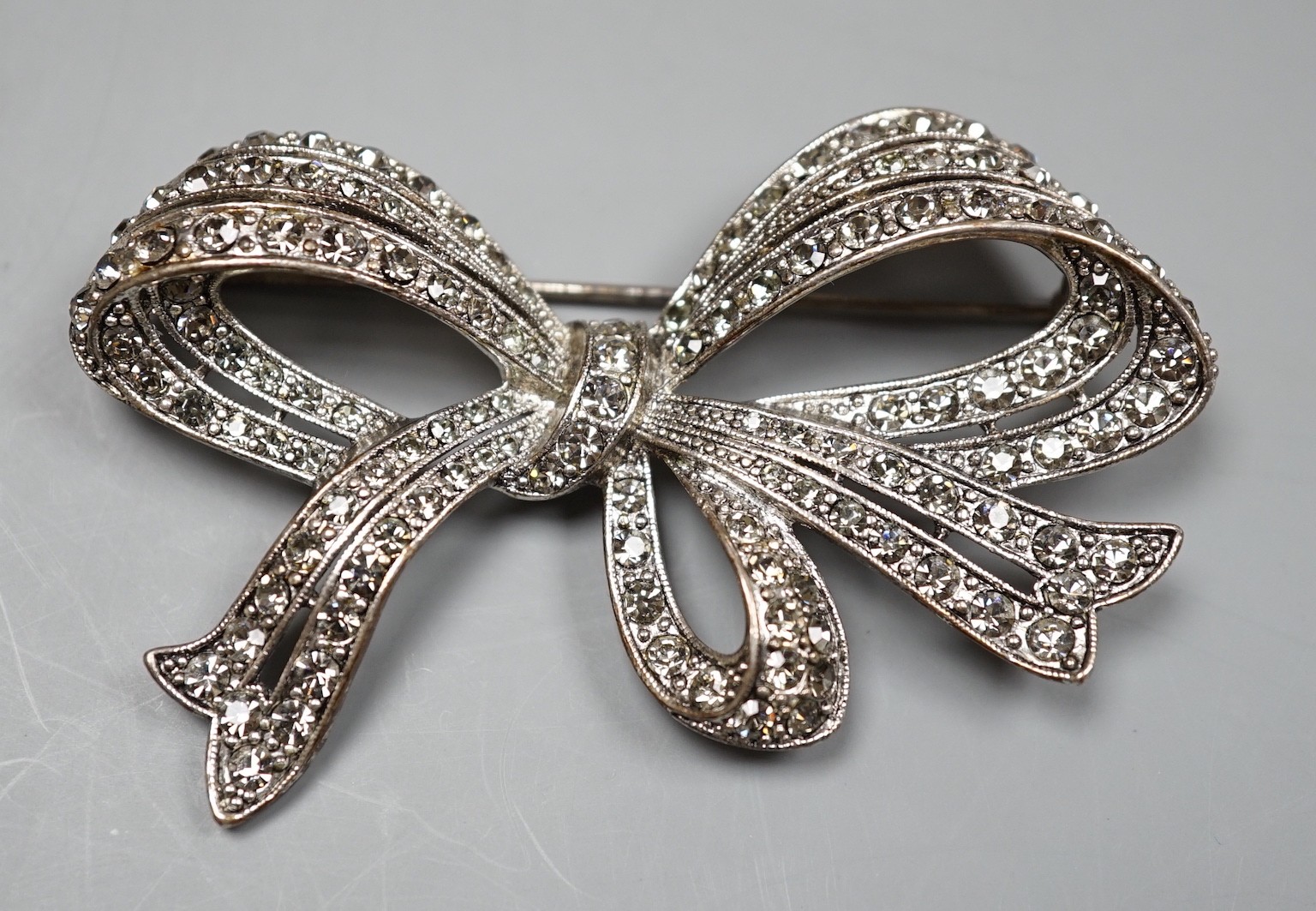 A white metal and paste set ribbon bow brooch, 77mm.